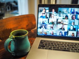 A coffee cup sits next to a laptop open to a virtual meeting with multiple individuals