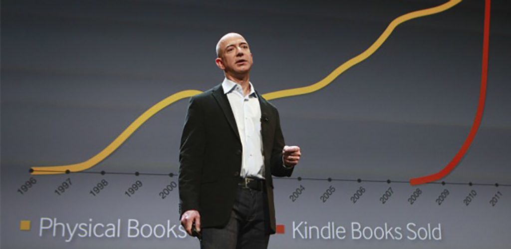 A photo shows Jeff Bezos flashing the slide showing the phenomenal growth of Amazonâs Kindle eBook sales in comparison to physical book sales during his presentation of the new Kindles.