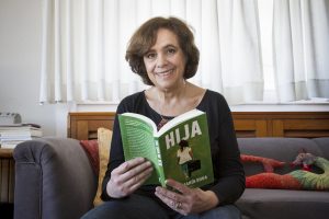 Una foto de la autora, sentada en un sofá, hojeando su libro "Hija"