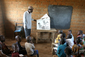 Un instituteur à un école primaire dans l'ouest de l'Afrique est debout en face des élèves assis. Il enseigne une leçon.