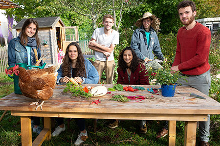 six jeunes adultes sont autour d'une table dehors avec une poule et des plantes
