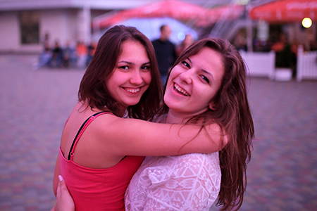 Deux femmes dansent en plein air et sourient à l'appareil photo. Elles se serrent dans les bras.