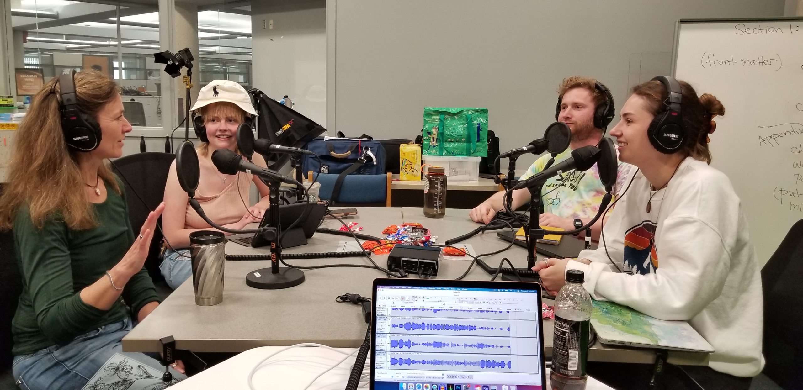 Group of 4 people sitting at table and conducting a podcast.