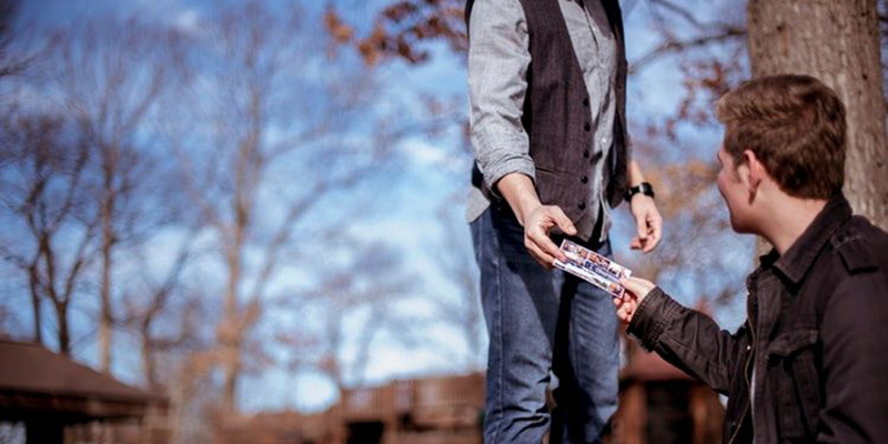 man sitting by a tree being handed something