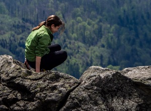 girl crouching on a cliff looking down.