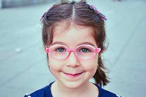 a little girl is smiling and wearing pink glasses with oval frames.