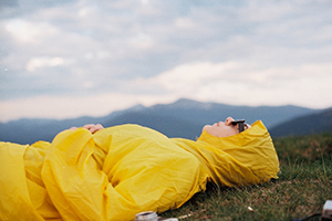 woman in raincoat lying on grass in the mountains