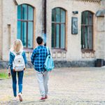 man and woman wearing backpack approaching large stone building