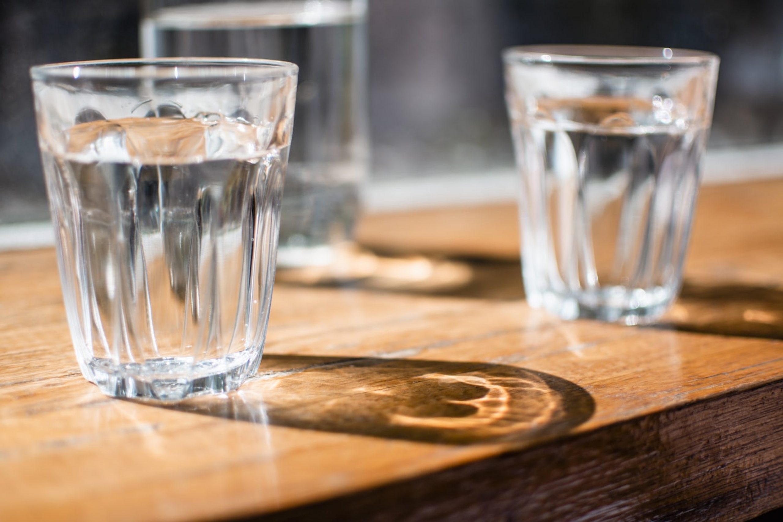 Two classes of water next to each other on a wooden table.