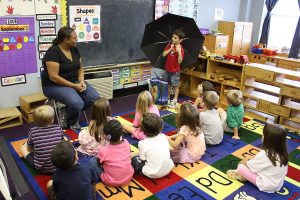 A boy displays an umbrella to his seated classmates for a session of Show and Tell.