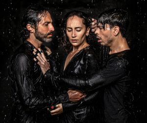 female surrounded closely by two men all in black and dripping wet in rain