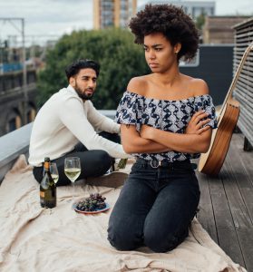 Woman turns back on male date, arms folded, kneeling on picnic blanket.