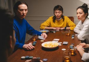 Three stern friends surround poker player at table.